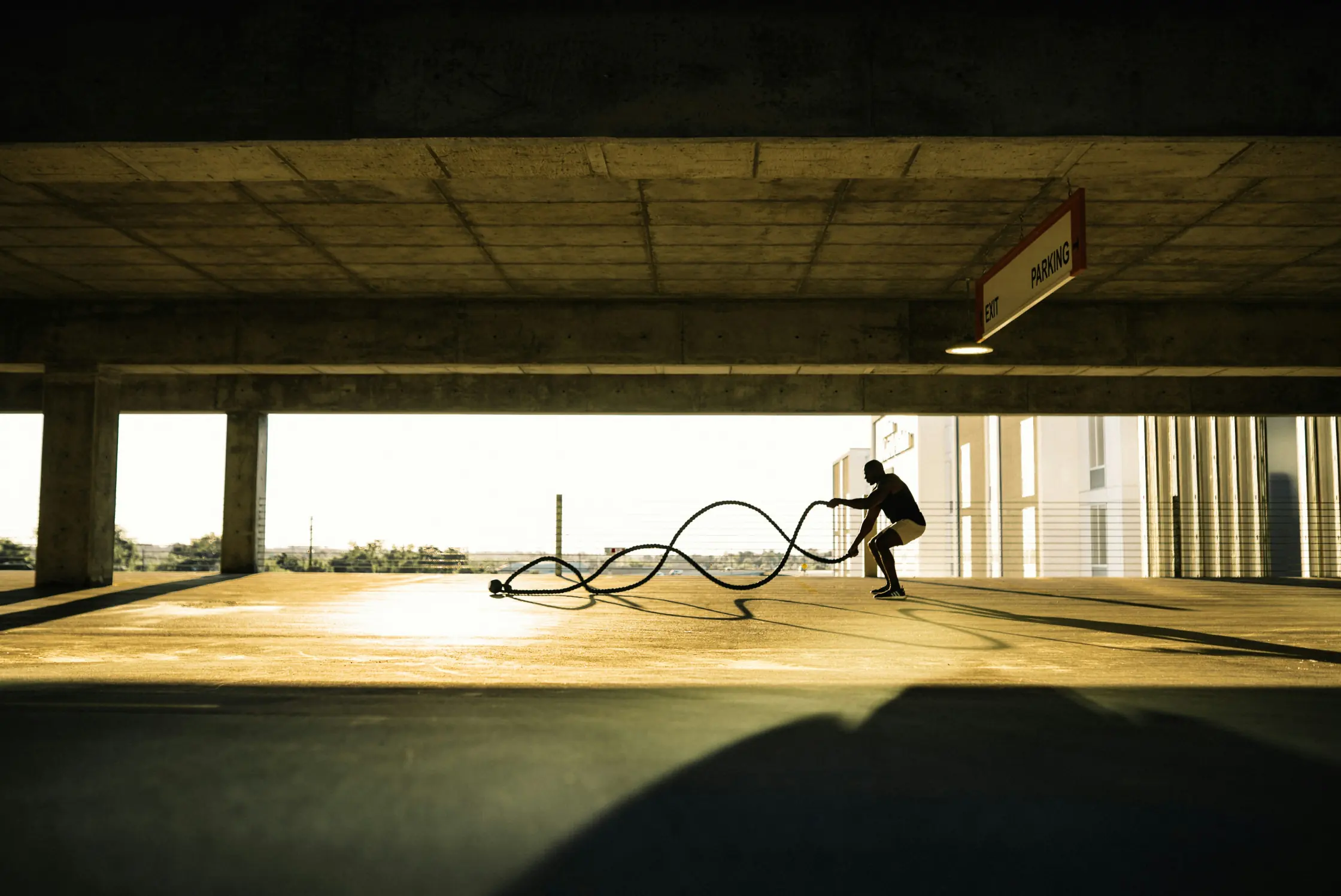 An athlete training alone on an empty parking deck at sunrise, in silhouette against the light.